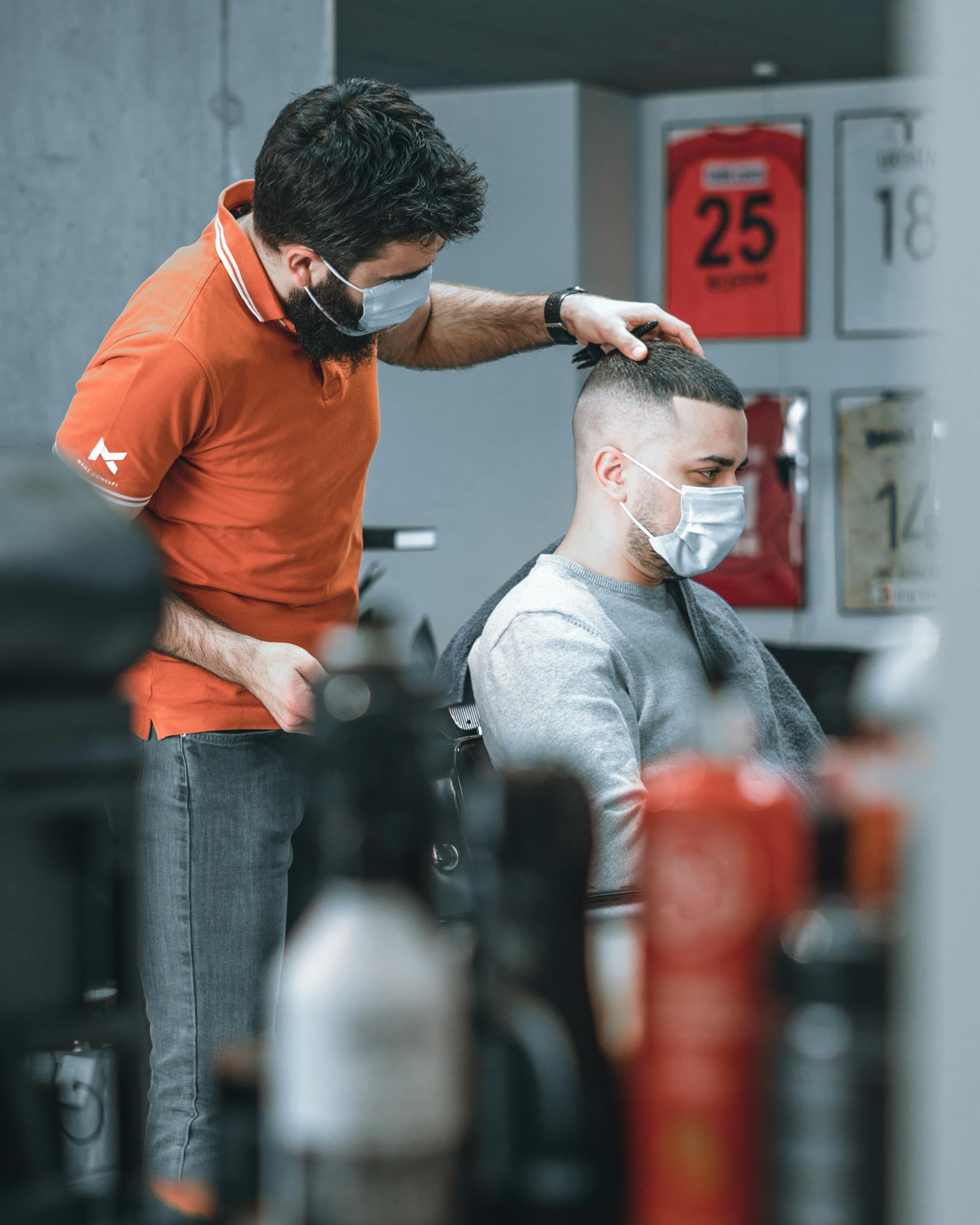 A barber wearing a face mask gives a haircut to a customer in a modern barbershop.