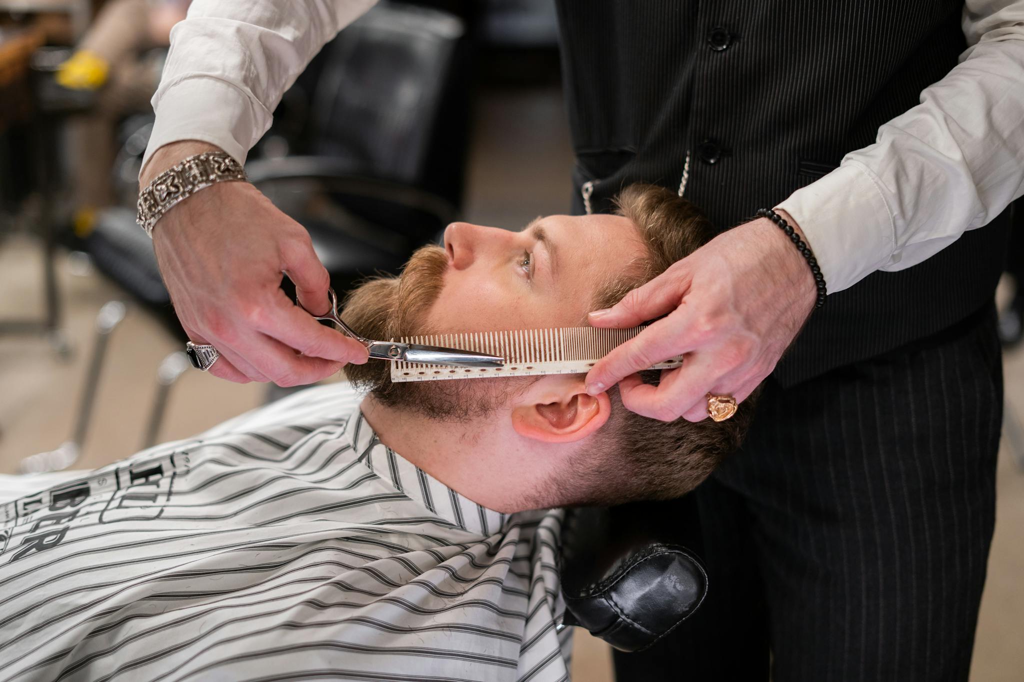 A skilled barber meticulously trims a client's beard using comb and scissors in a modern barbershop.